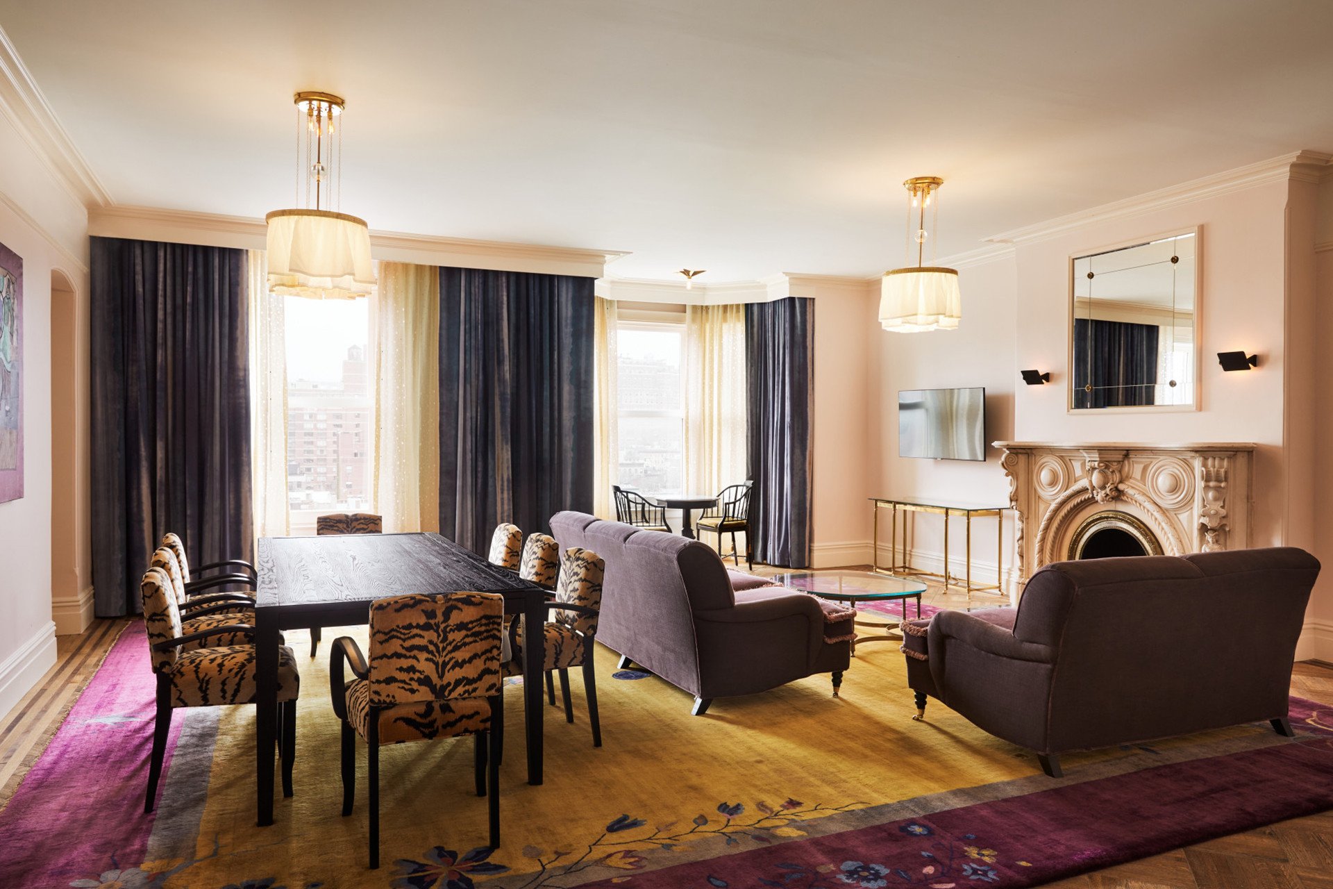 A large room with a dining table, seating area, fireplace, and city view.